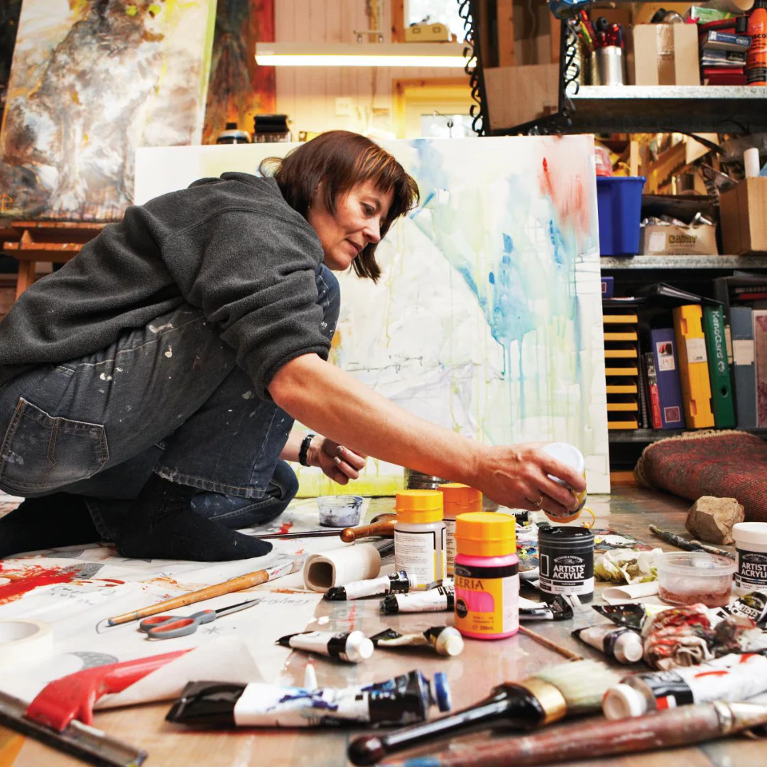 Artist working in studio surrounded by paints and canvases
